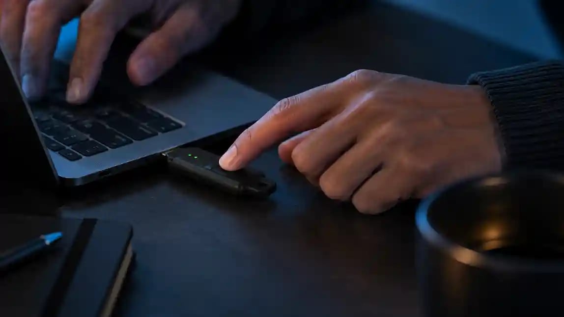 Hand pressing the fingerprint sensor on a Token BioStick plugged into a laptop
